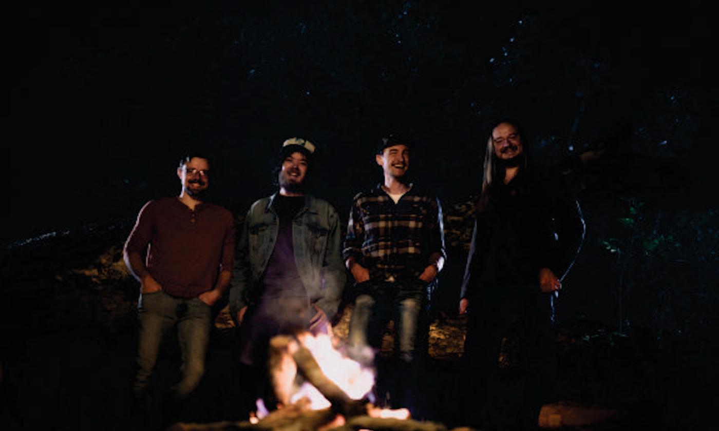 Tophouse stands near a burning fire-it and smiles for the camera. 