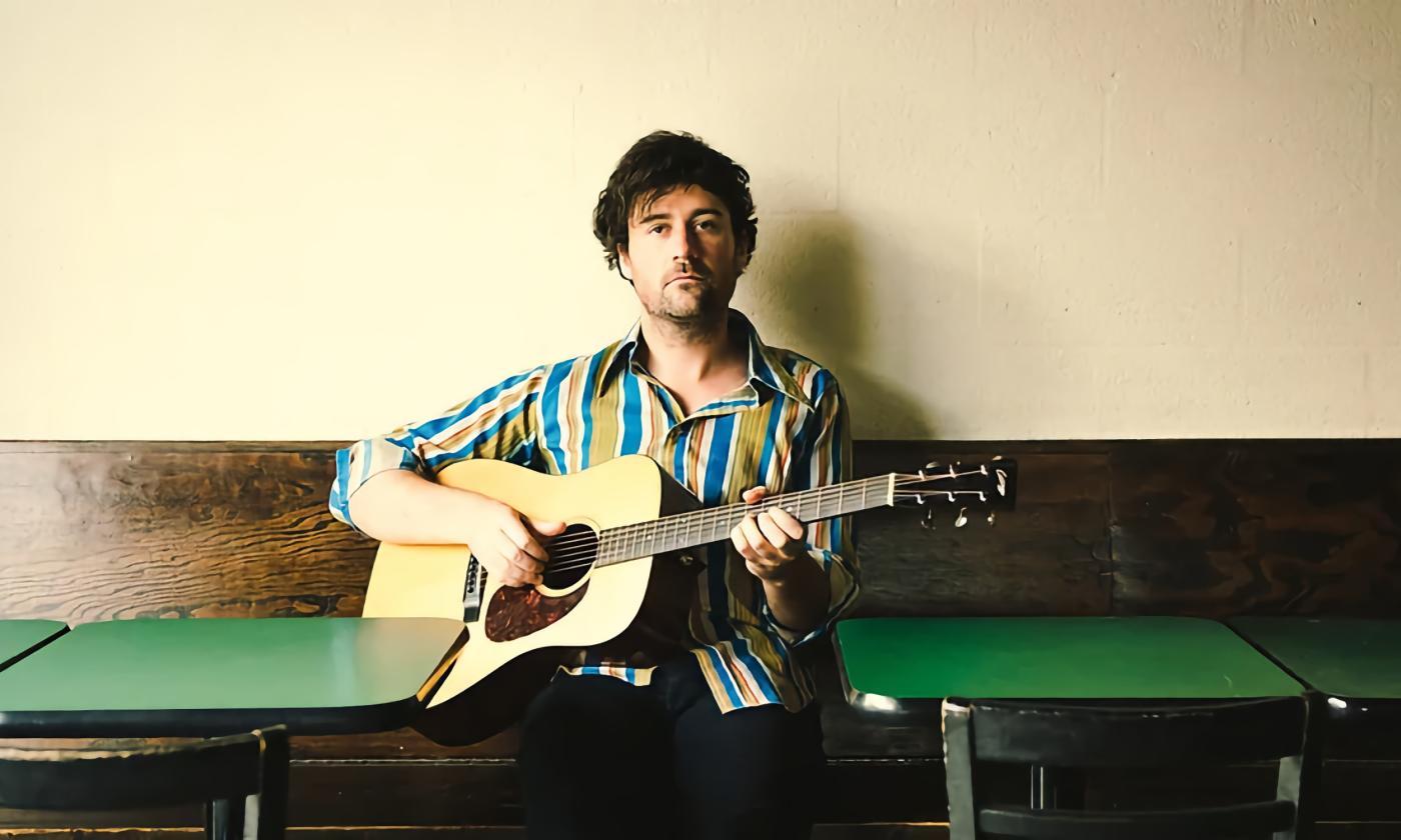 Jordan Tice, sitting with his guitar at a diner with green-topped tables