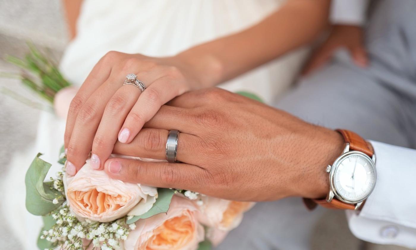 Newlywed couple's hands clasped together over a bouquet of peach roses and baby's breath