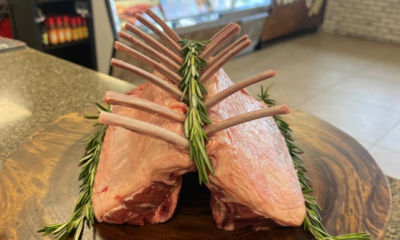 A rack of raw lamb with rosemary sprigs, artistically arranged and presented on a round wooden board