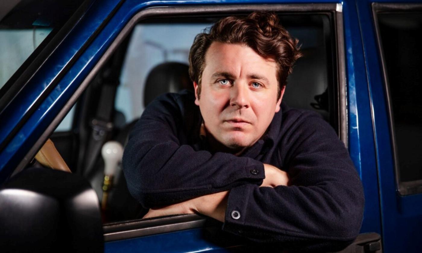 Joe Pug poses in a blue vehicle. 