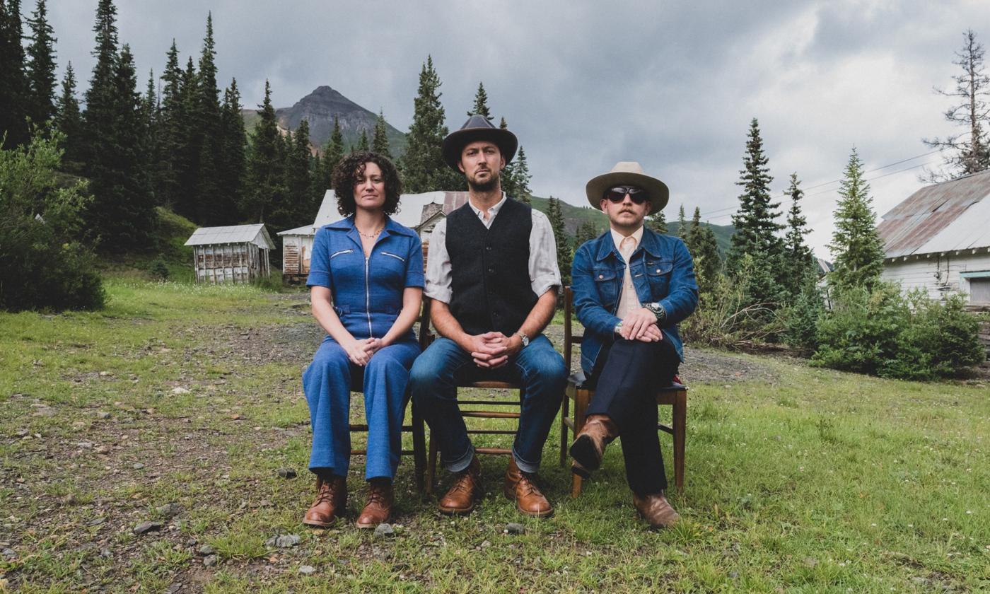 Bandmates from Stillhouse Junkies pose on a bench in front of a group of houses and trees.