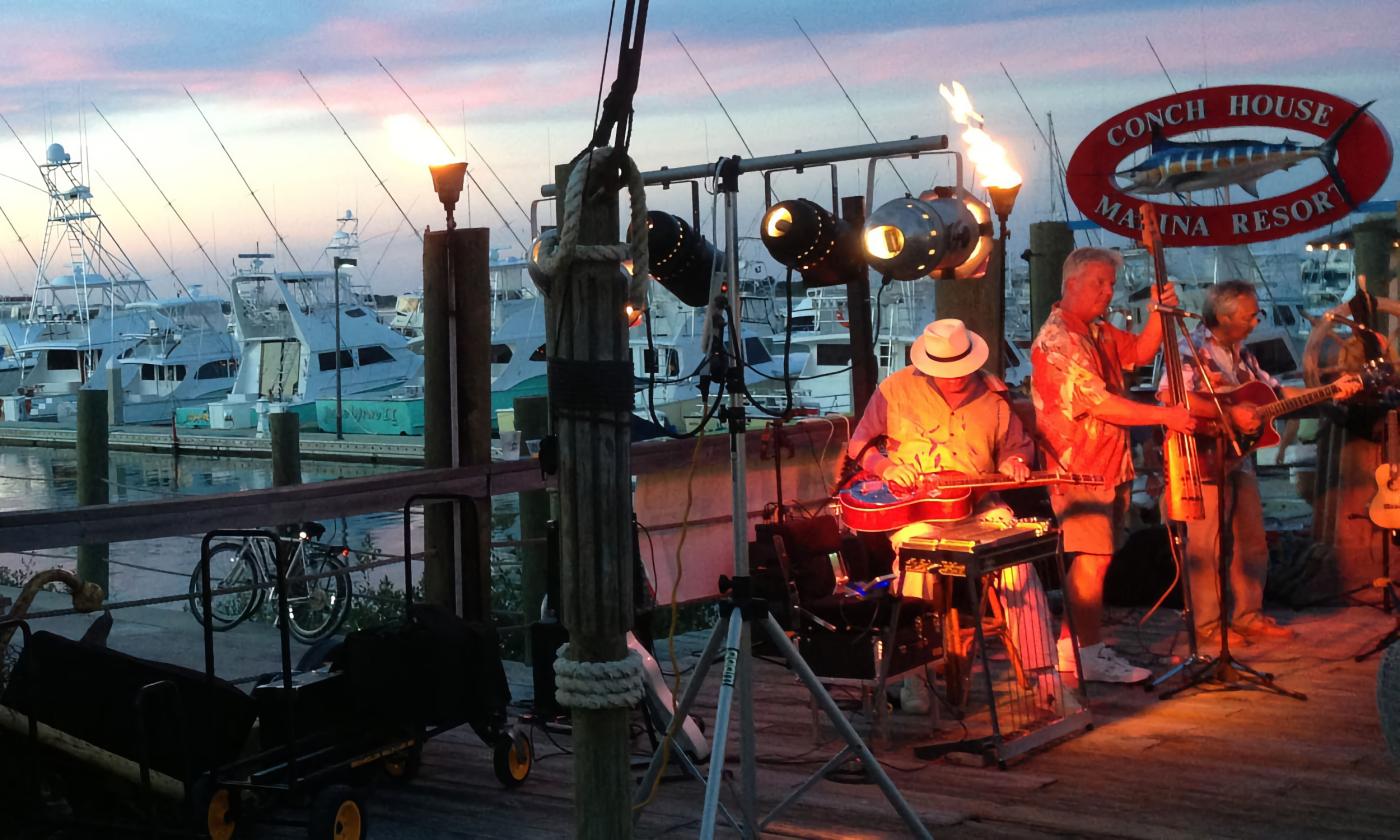 The three members of the band Big Pineapple on the deck at the Conch House at sunset