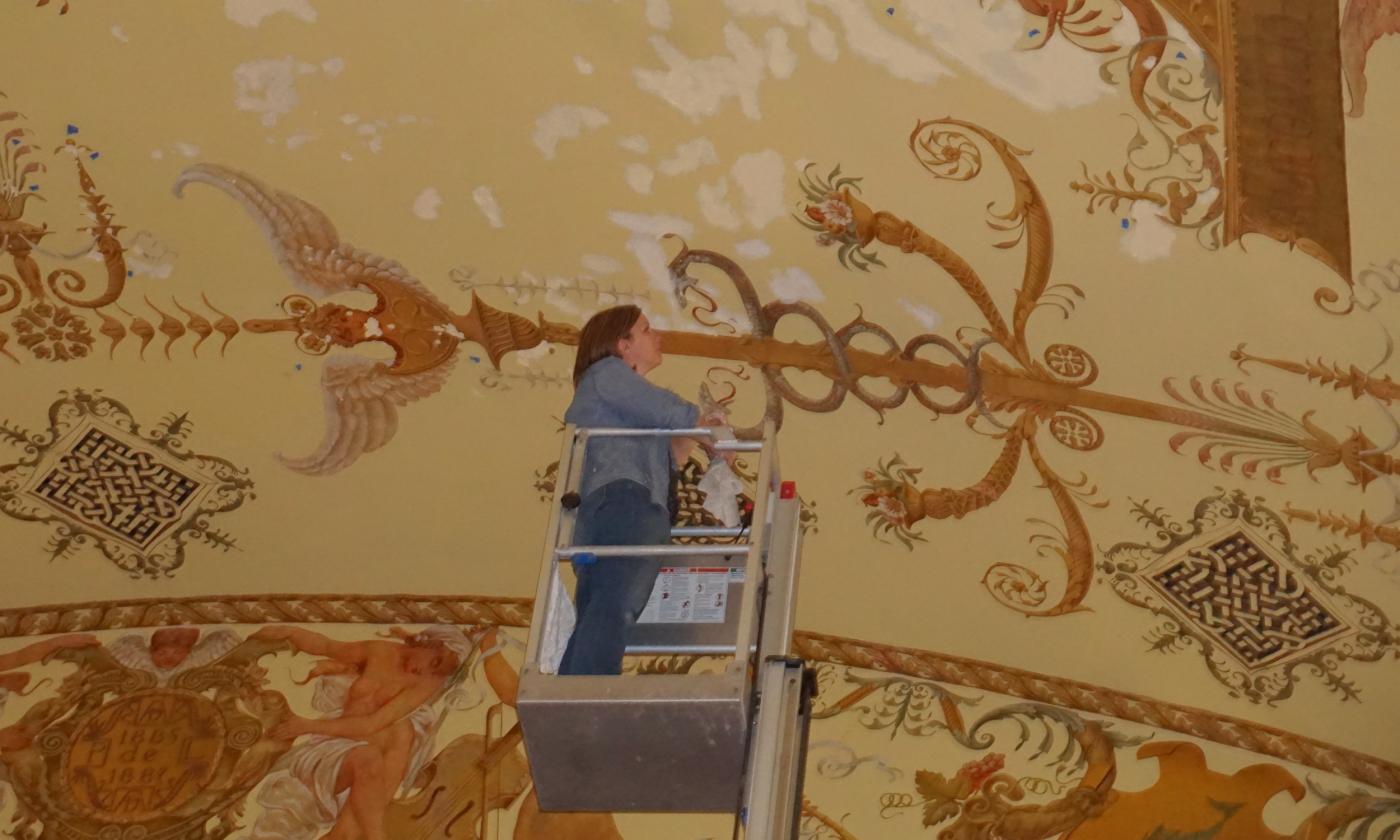 A woman stands in an interior construction lift, while restoring gilded-age decor at Flagler College