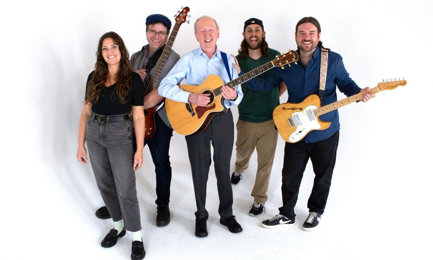 Al Stewart and his bandmates clutch their guitars and pose in front of a white backdrop.