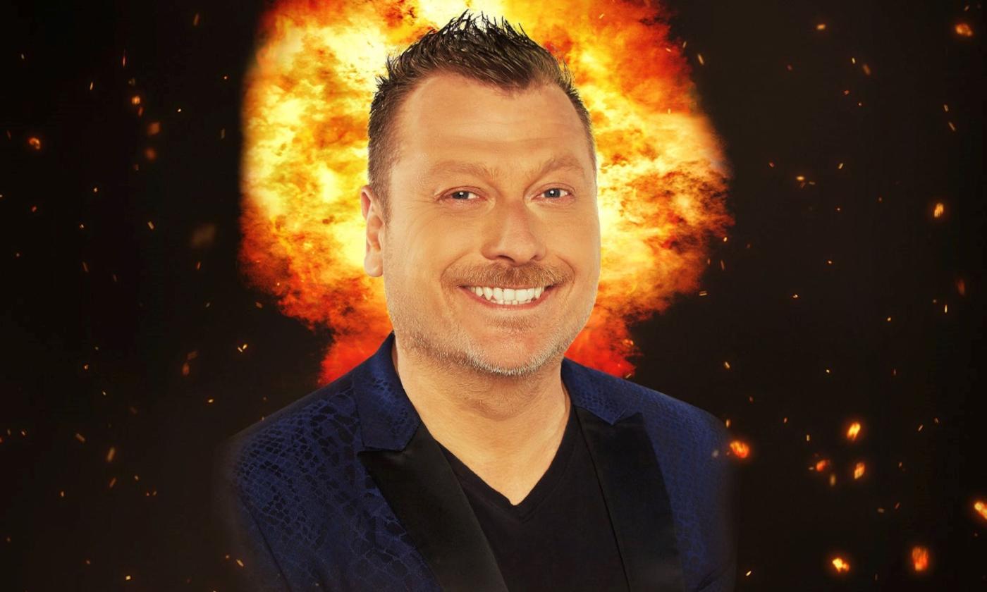 Jimmy Failla smiles and poses in front of a black backdrop with flames.