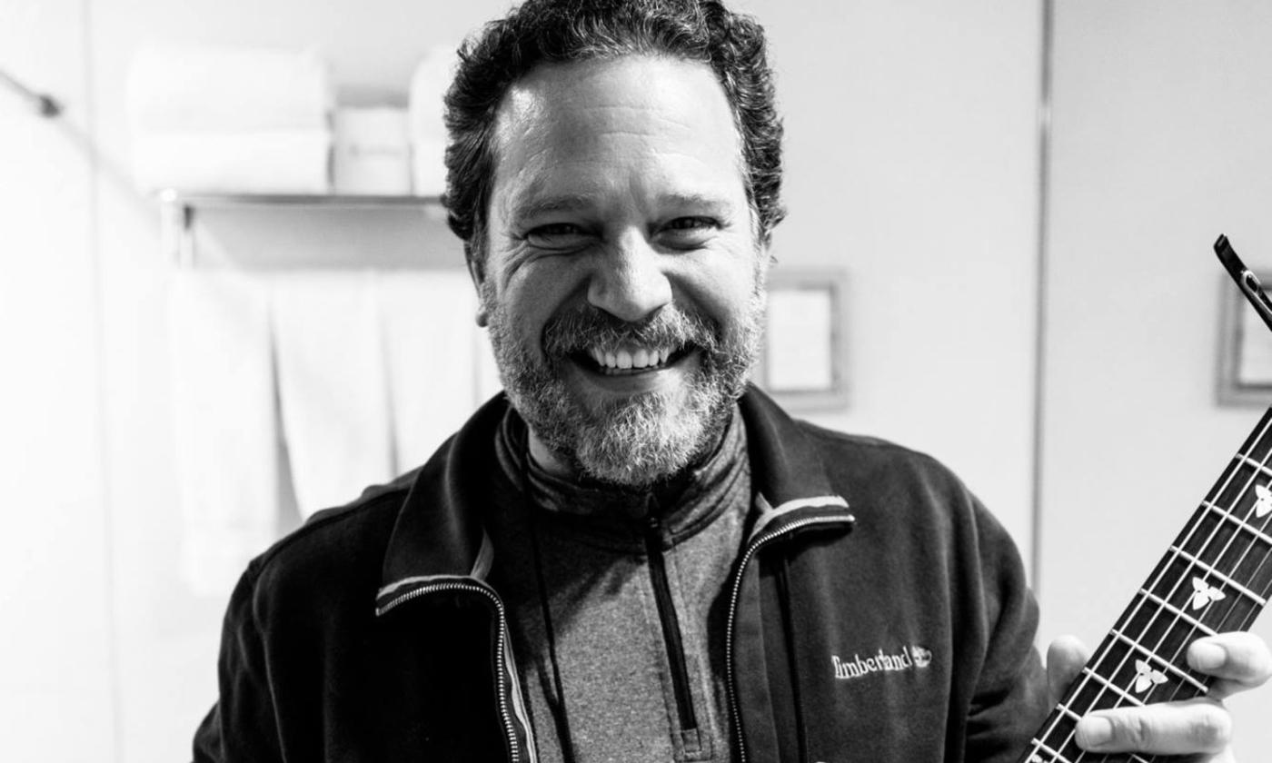 Marc Douglass Berardo smiles while holding onto his guitar.