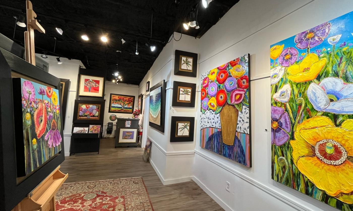 The gallery space of Maria Reyes-Jones. Walls are lined with huge, brightly colored paintings of flowers. An easel stands in the foreground.