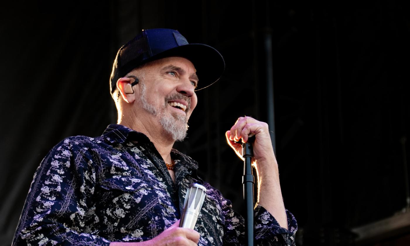 JJ Grey on stage holding a microphone wearing a ball cap and a blue and black shirt