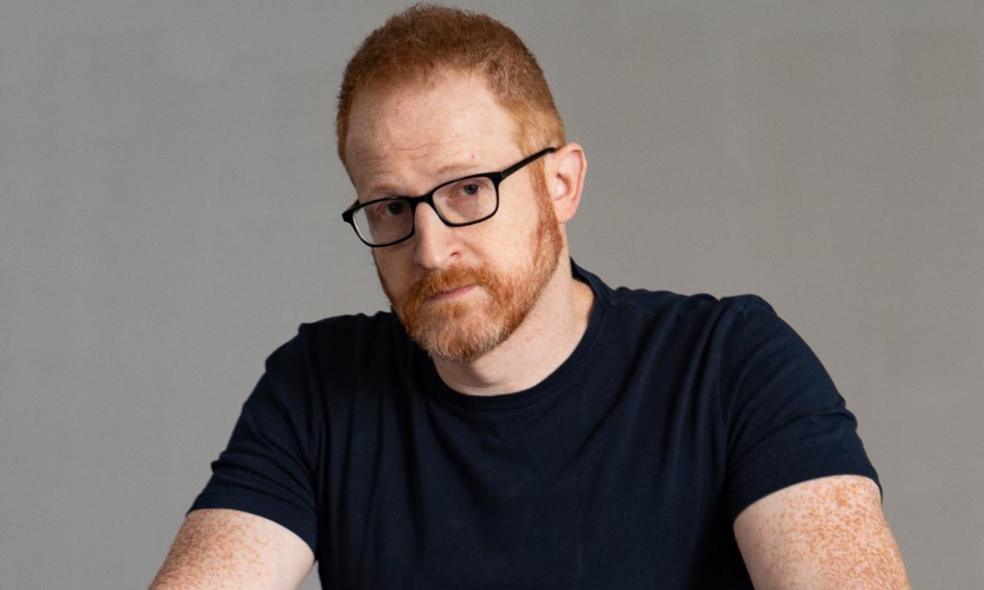 Steve Hofstetter wears glasses and a black t-shirt while posing in front of a grey backdrop.