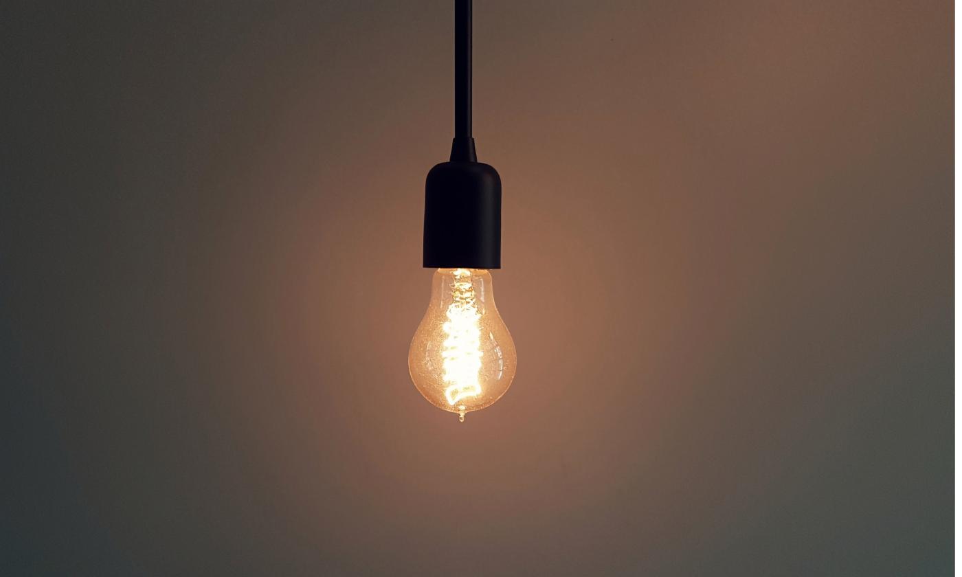 A bare, lit lightbub hangs from a ceiling in a darkened room