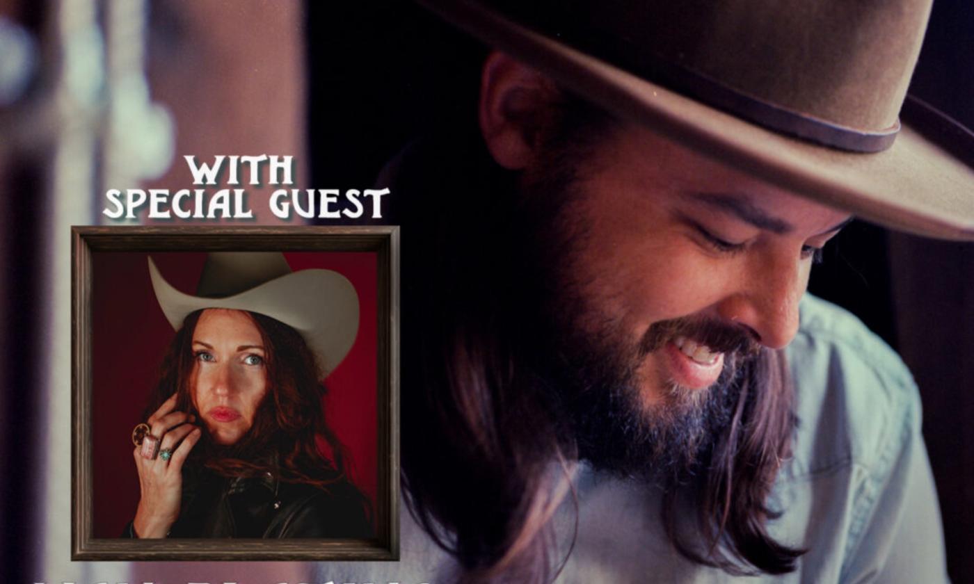 Caleb Caudle poses and smiles while wearing a brown hat and a blue shirt. 