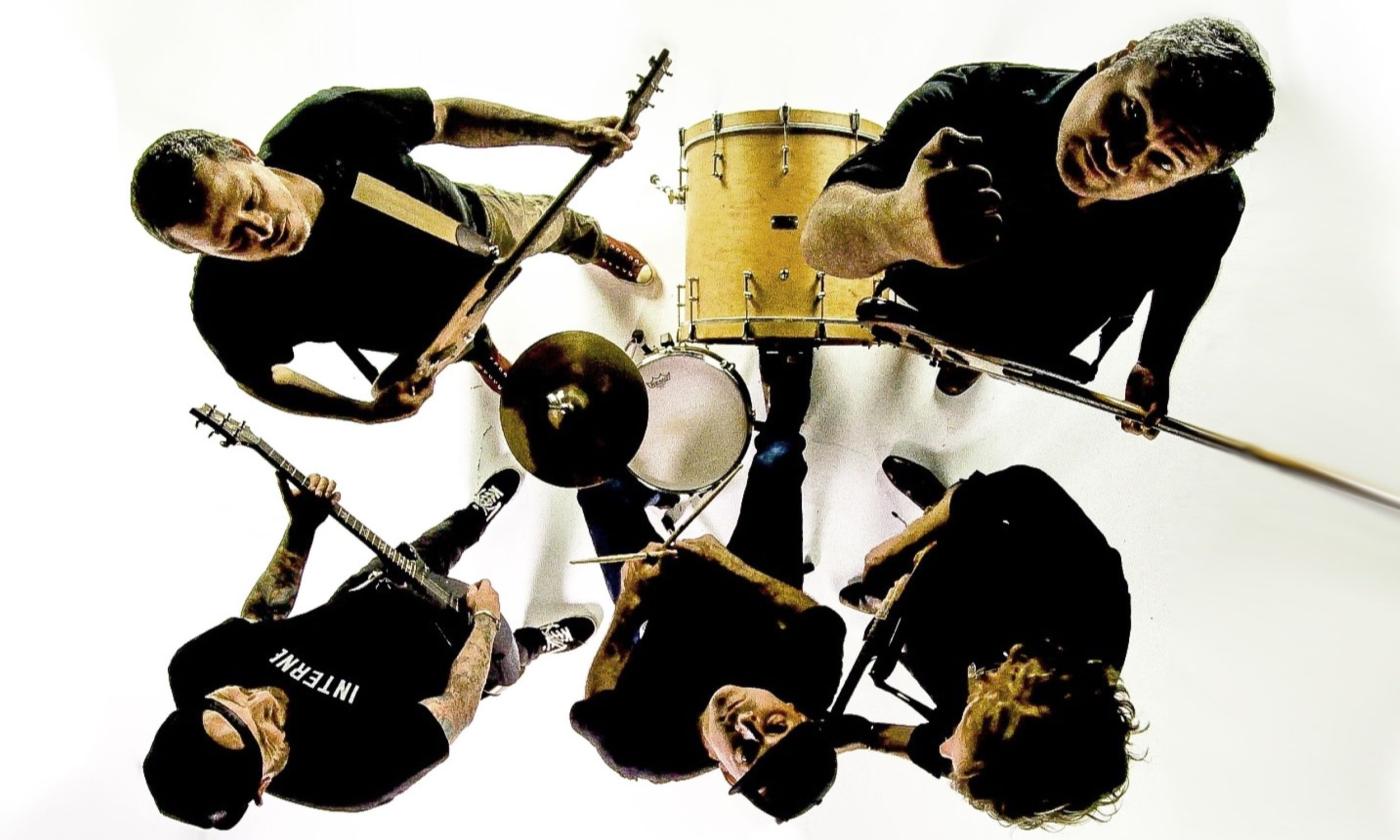 Bandmates from Jimmie's Chicken Shack play with their musical instruments in front of a white backdrop. 