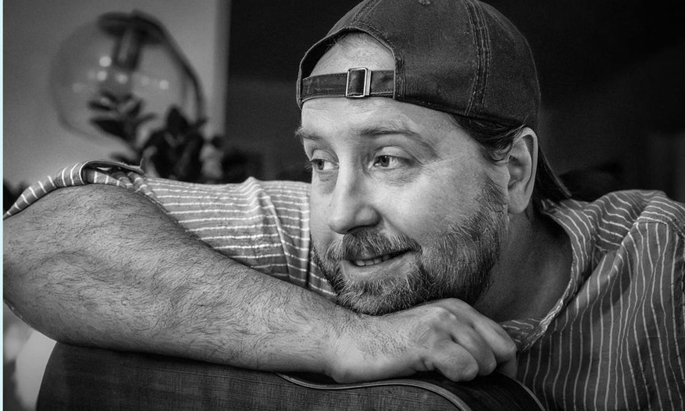 musician Jim Johnston in a ball cap, leaning on his guitar