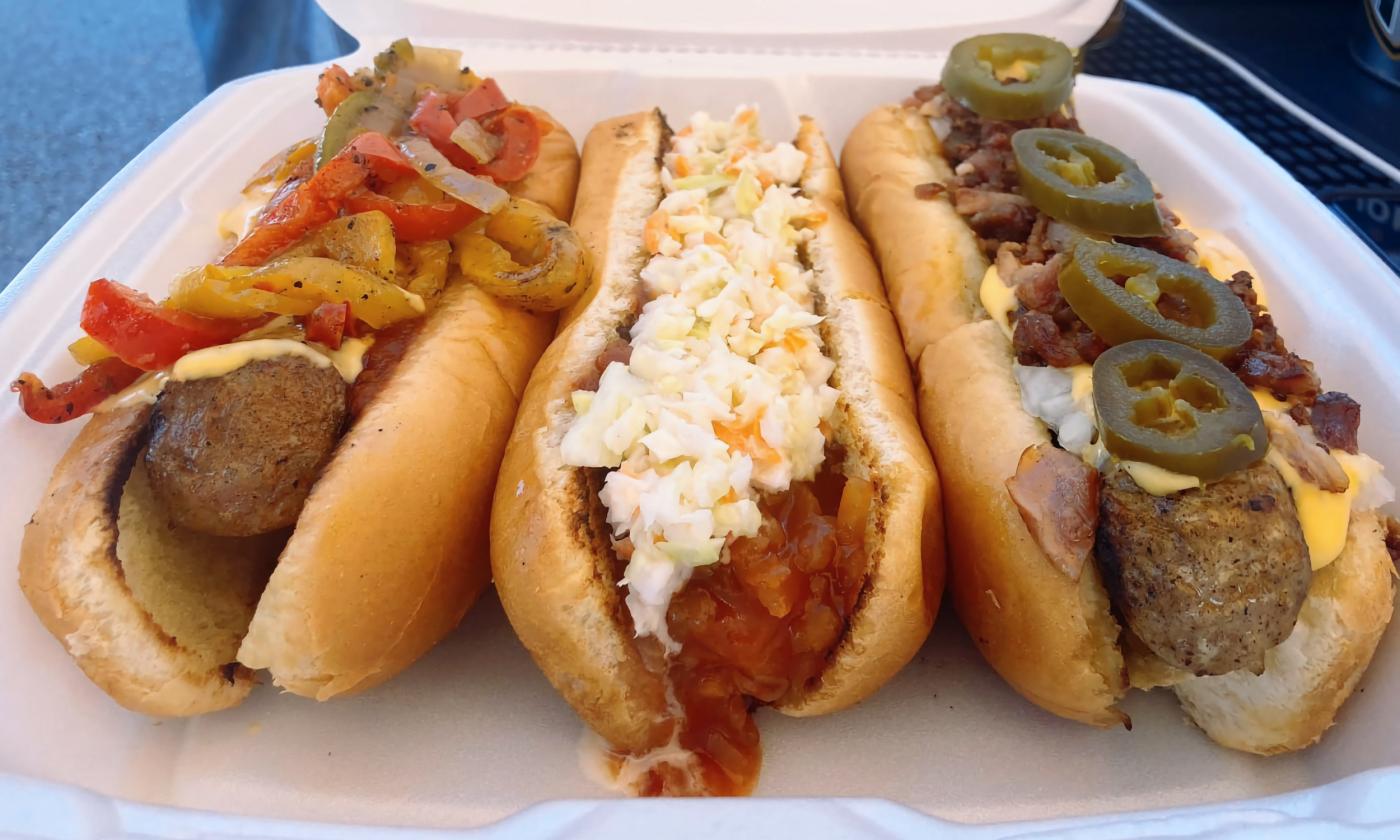 A tray of dogs with slaw, jalapeños, onions, peppers, and additional toppings