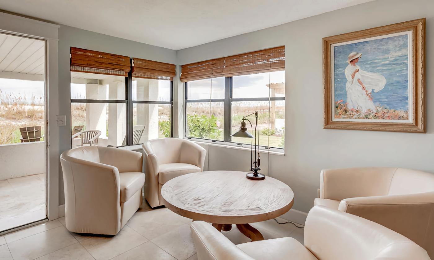 A round table, with four swivel chairs, and a view of dunes and ocean in an oceanside cottage