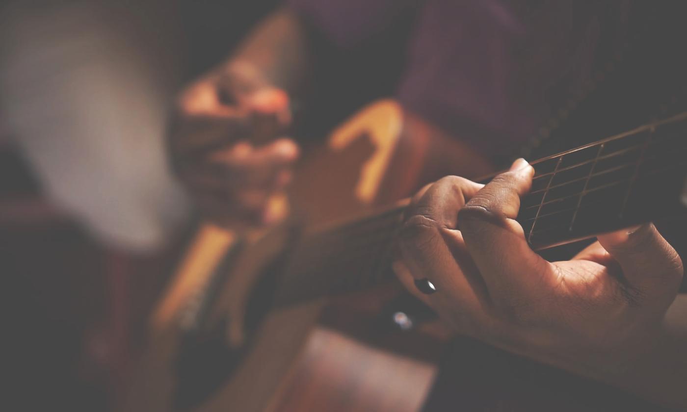 Focused on two hands as they play an acoustic guitar