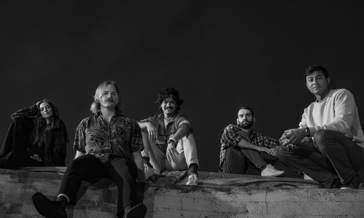 Madwoman, a five-member band, arrayed seated on a wall against a black sky