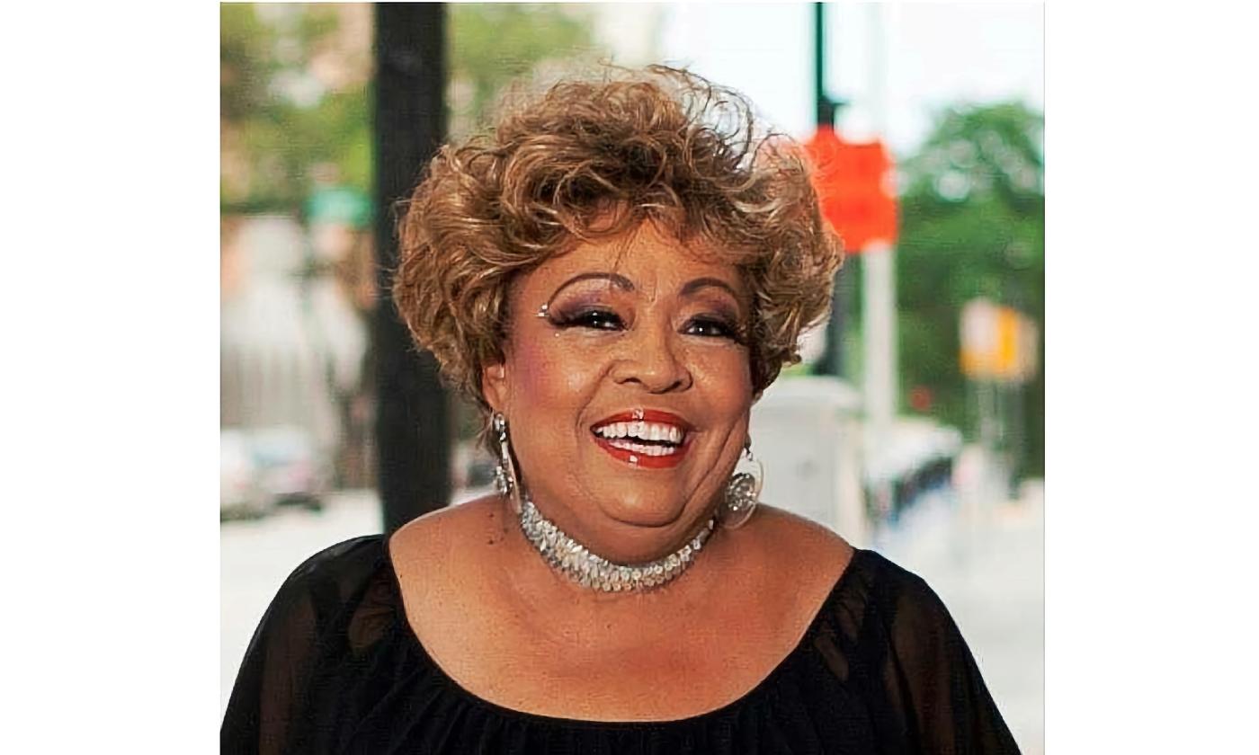 Linda Cole, smiling at a gig, wearing a black top, sparkling necklace and a lovely smile.