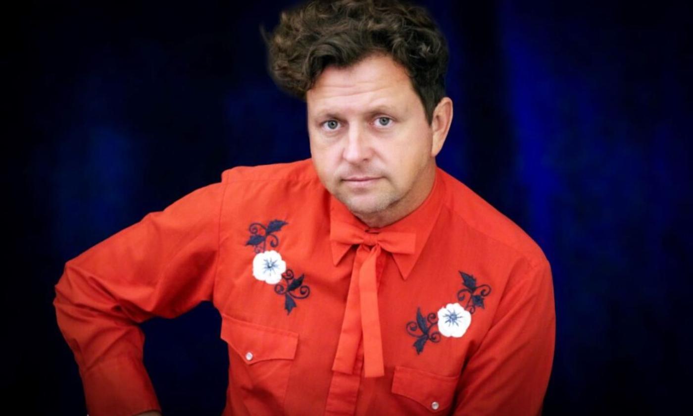 Abe Partridge poses in an orange shirt in front of a blue backdrop. 