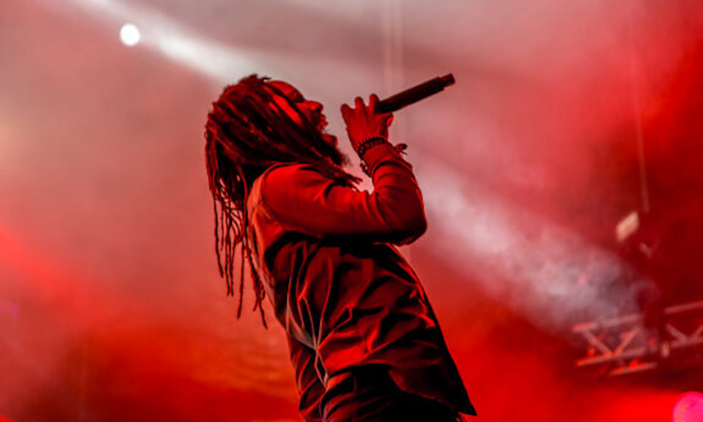 Kabaka Pyramid performs on a stage with a red backdrop. 