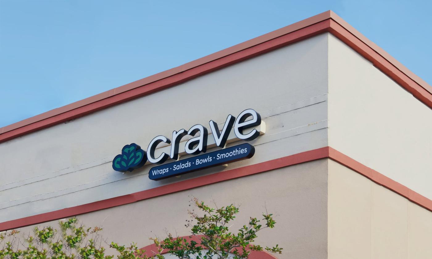 Looking upwards, a square roof line against a blue sky. A sign reads "Crave."