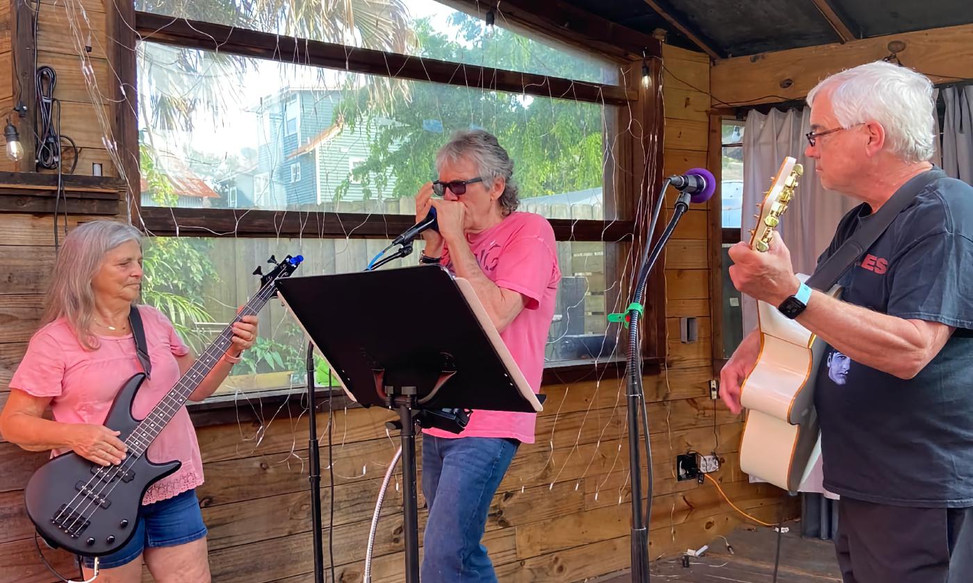Three musicians, a bass player, harmonica player, and guitarist performing together at an open mic