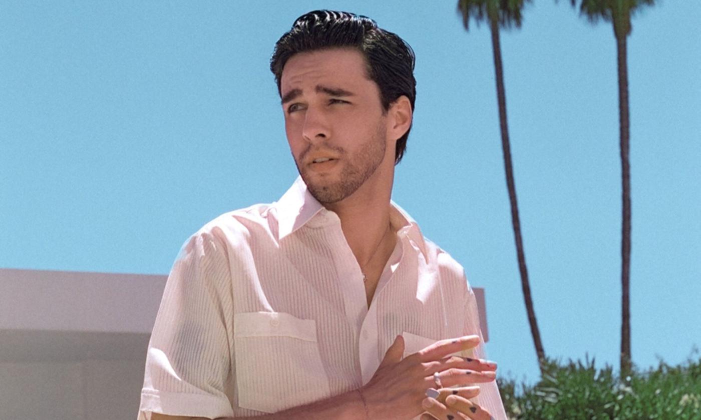 Stephen Sanchez wears a white dress shirt and poses in front of two palm trees.