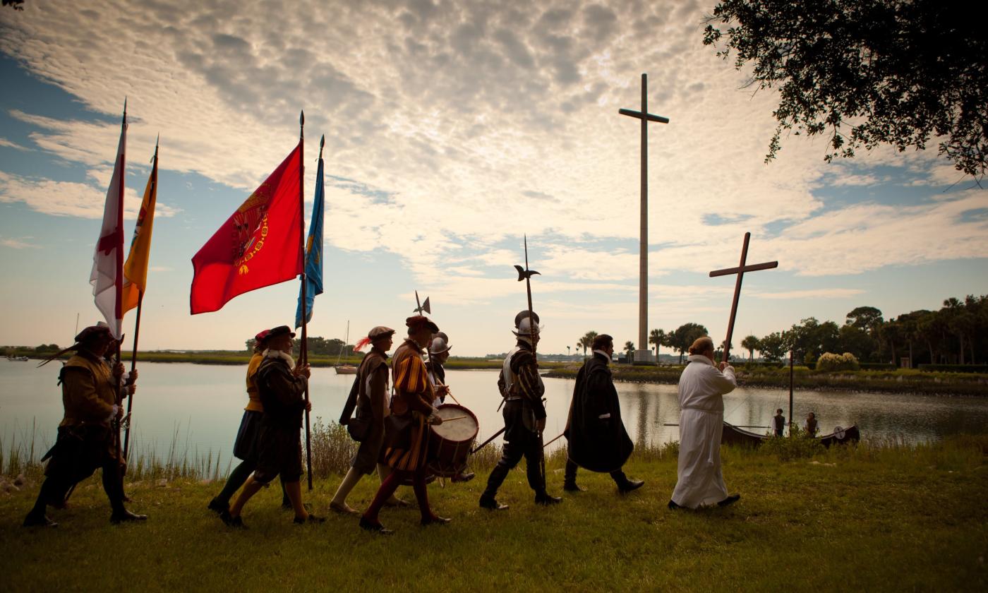 Seven men walk in a procession along the Matanzas River, dressed in the garb of colonial Spanish soldiers, citizens, and priests.