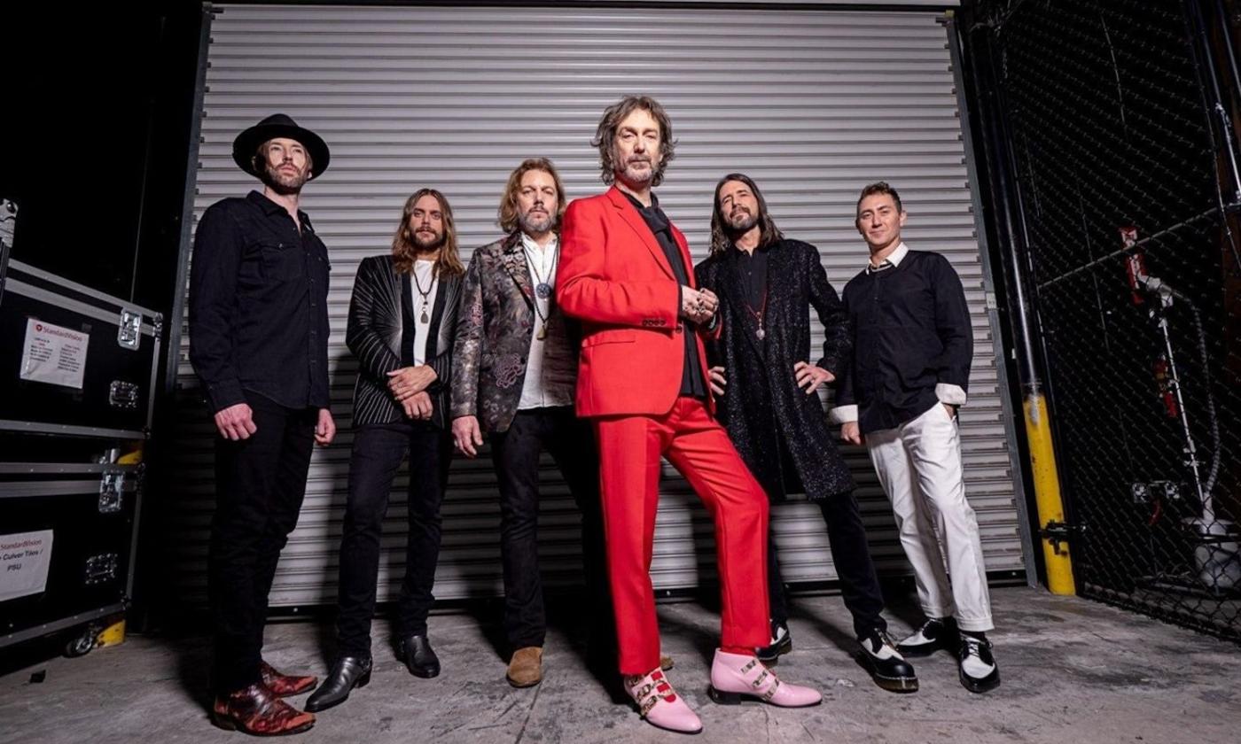Bandmates from The Black Crowes pose in black in front of a garage door.