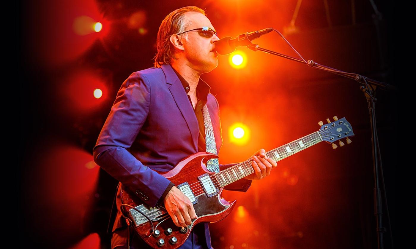 Joe Bonamassa wears a purple blazer and sings on stage for fans.