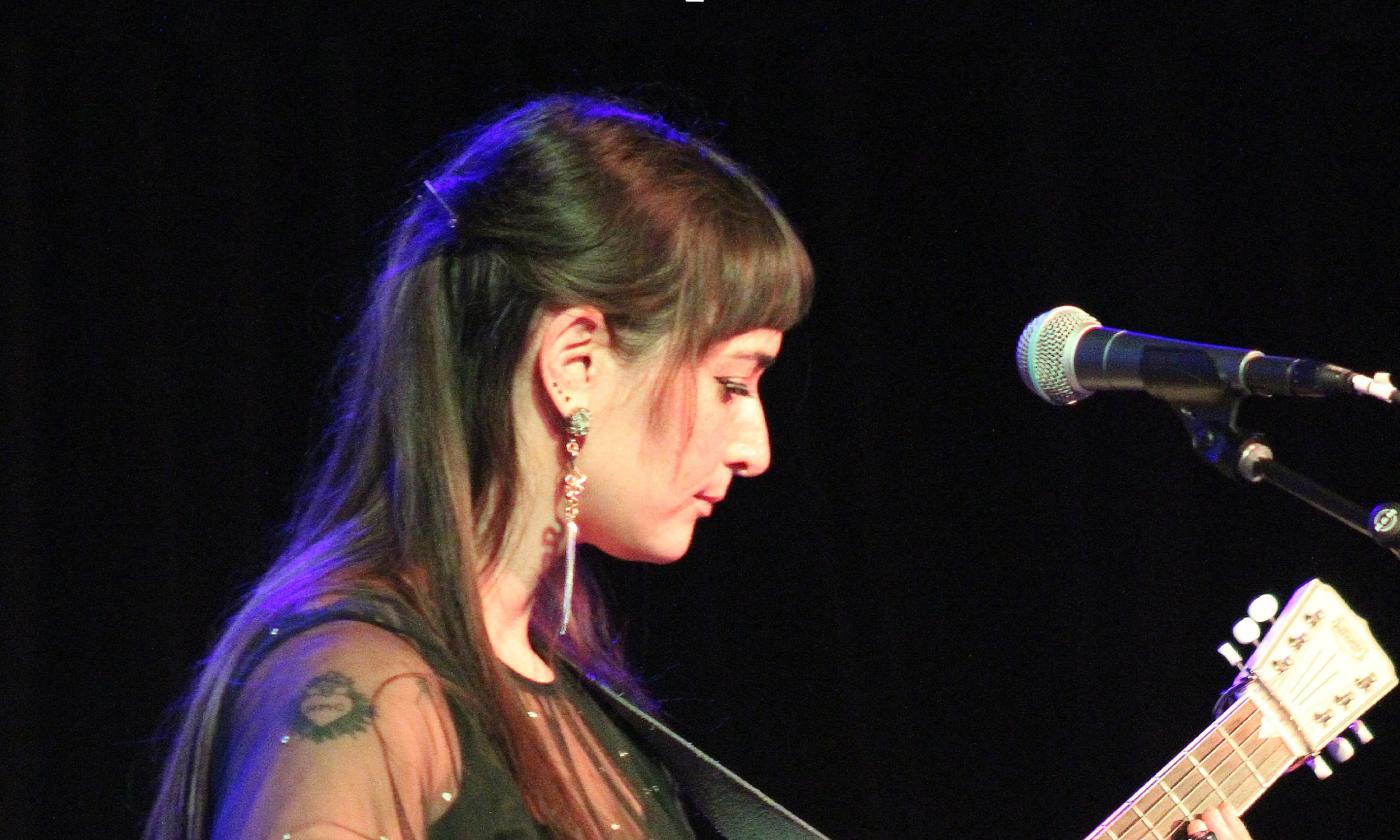 Cristina Vane, on stage wearing black, with her cream-colored resonator guitar