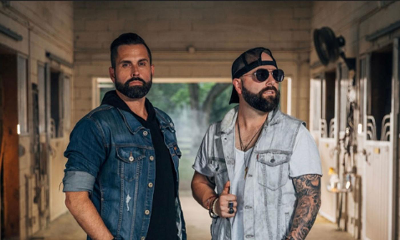 Country music duo, Chris James Band, standing in a stable.