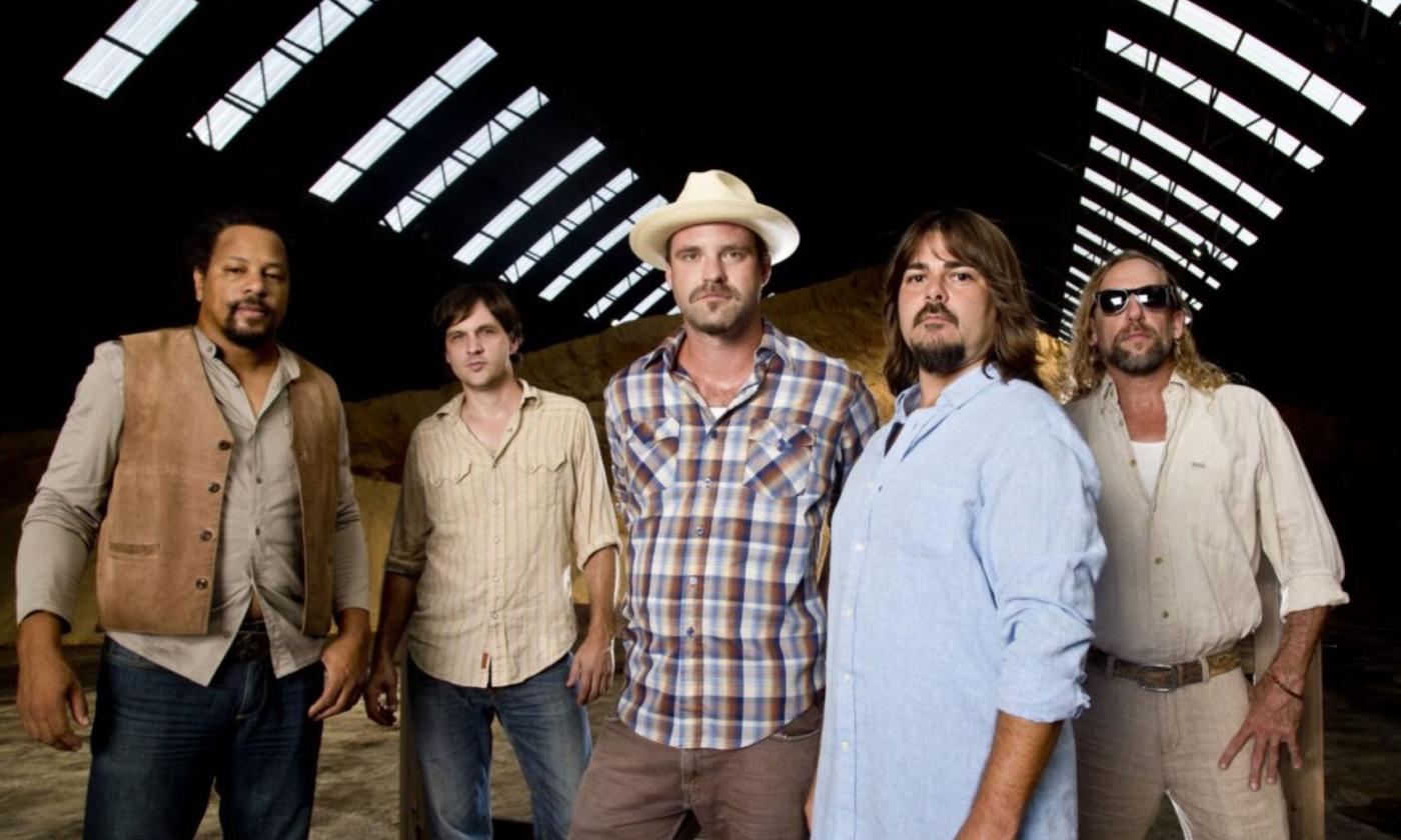 The members of Honey Island Swamp Band smile as they pose together inside a rustic barn.