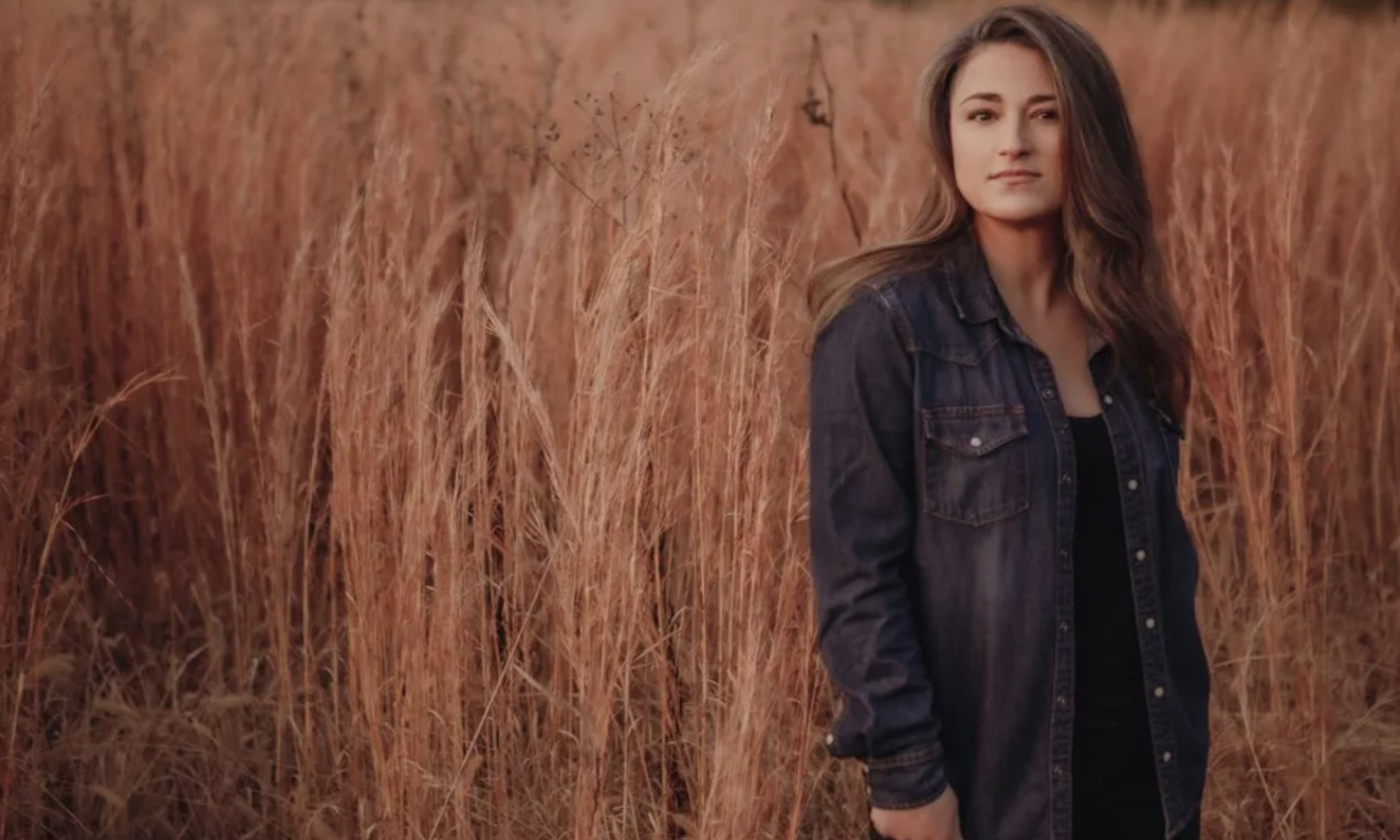 Jennifer Knapp stands against a backdrop of wheat, wearing a black jacket.