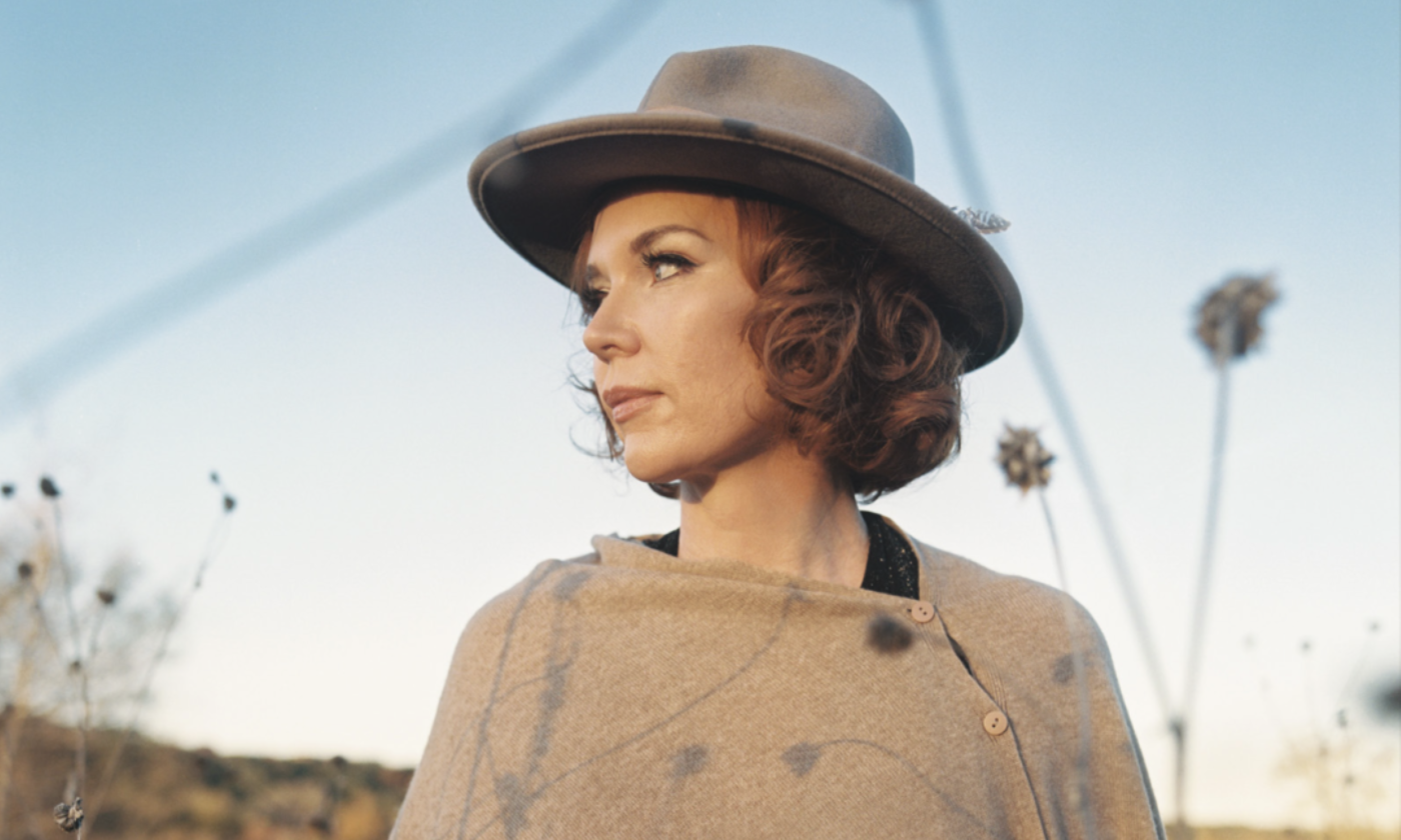 Sue Foley wears a hat and poses in a field with flowers.