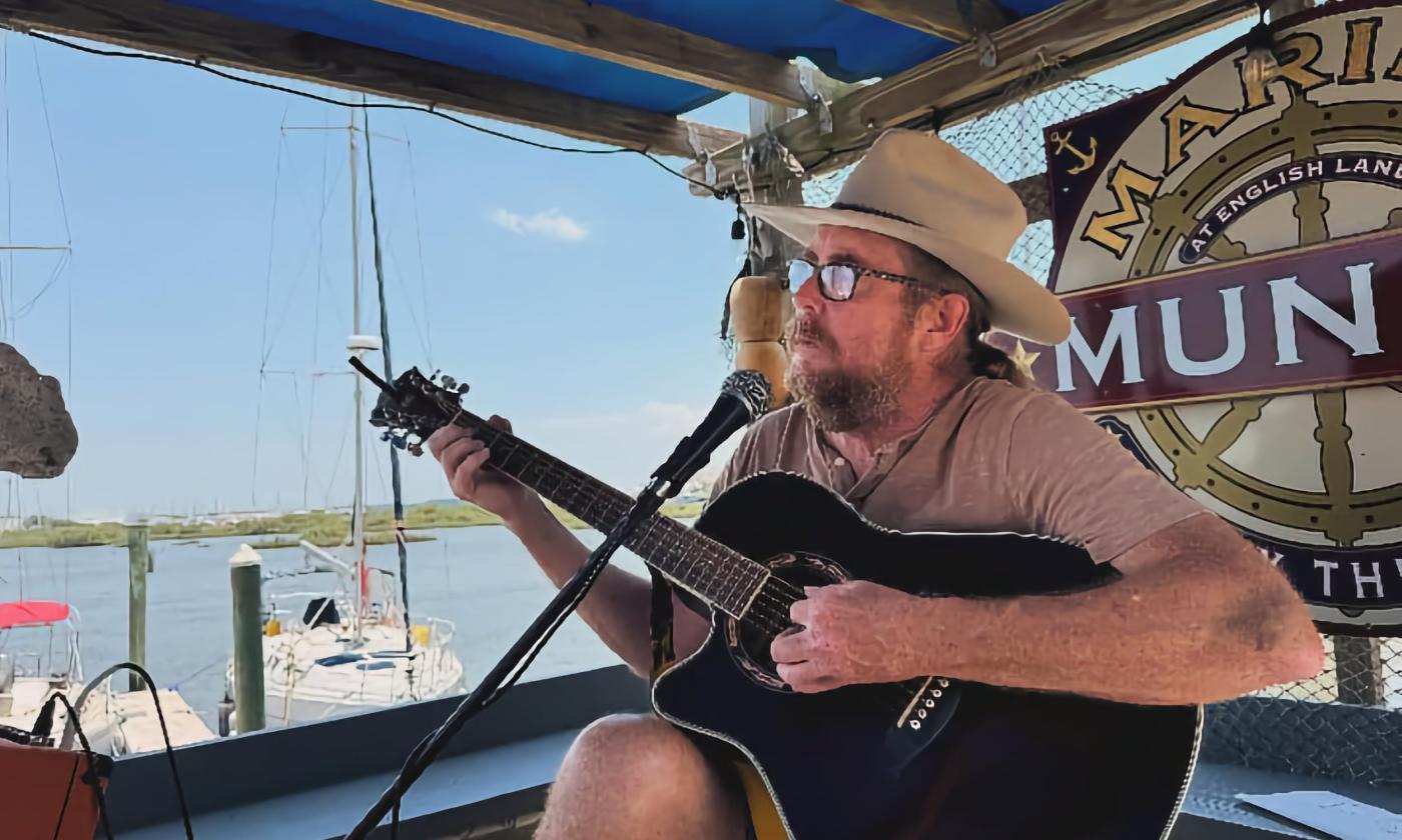 Musician Doug Hyde, with his guitar at Marina Munch on a blue-sky day