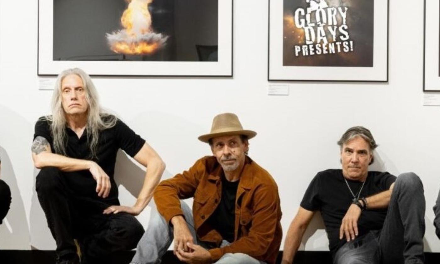 Bandmates from Given To Fly Pose in front of a white wall with framed posters.
