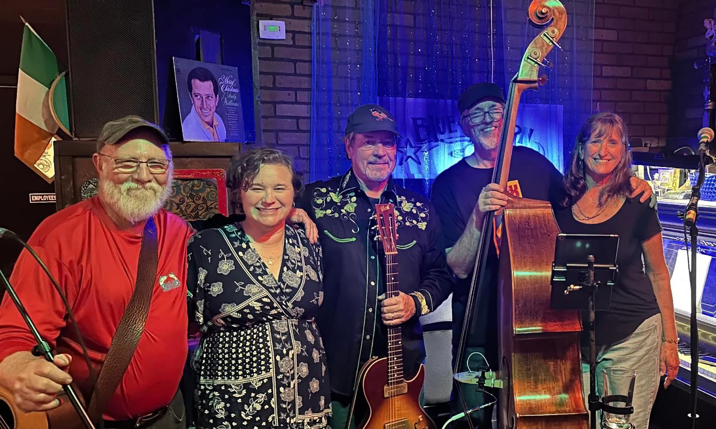The five members of Sawmill Jam standing with their instruments on a venue stage