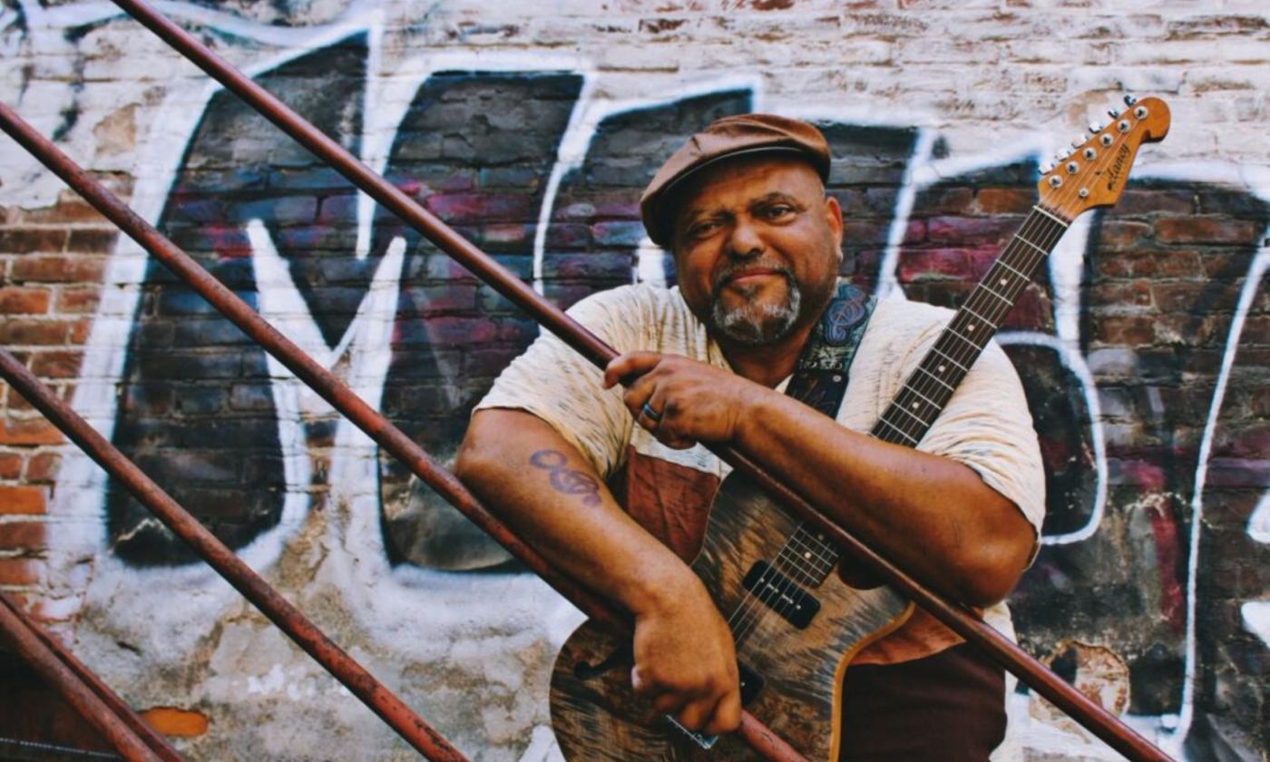 Kevin Burt clutches his guitar on a staircase with graffiti as a backdrop.