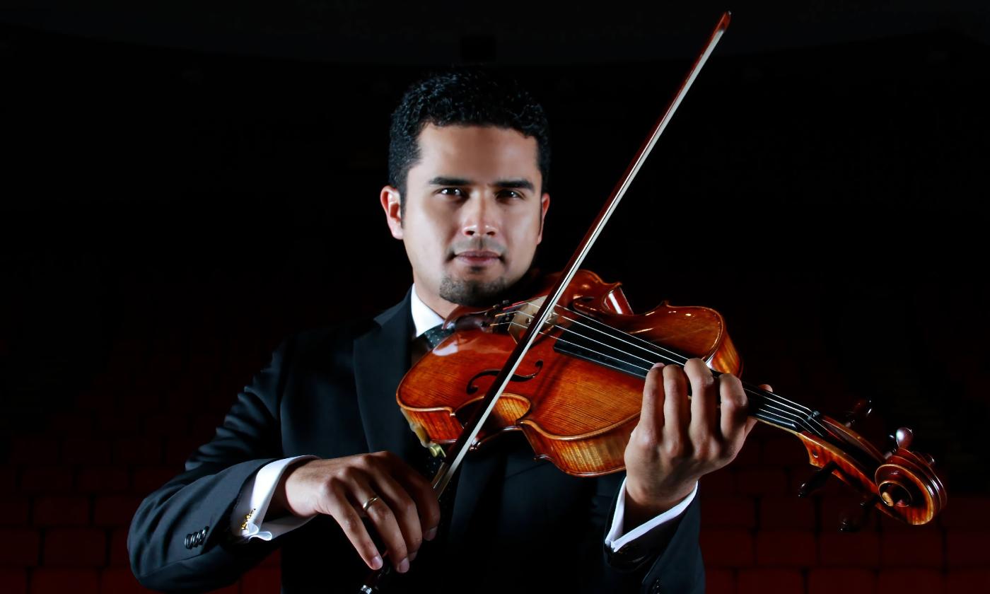 A man in a tuxedo, playing the viola against a black background