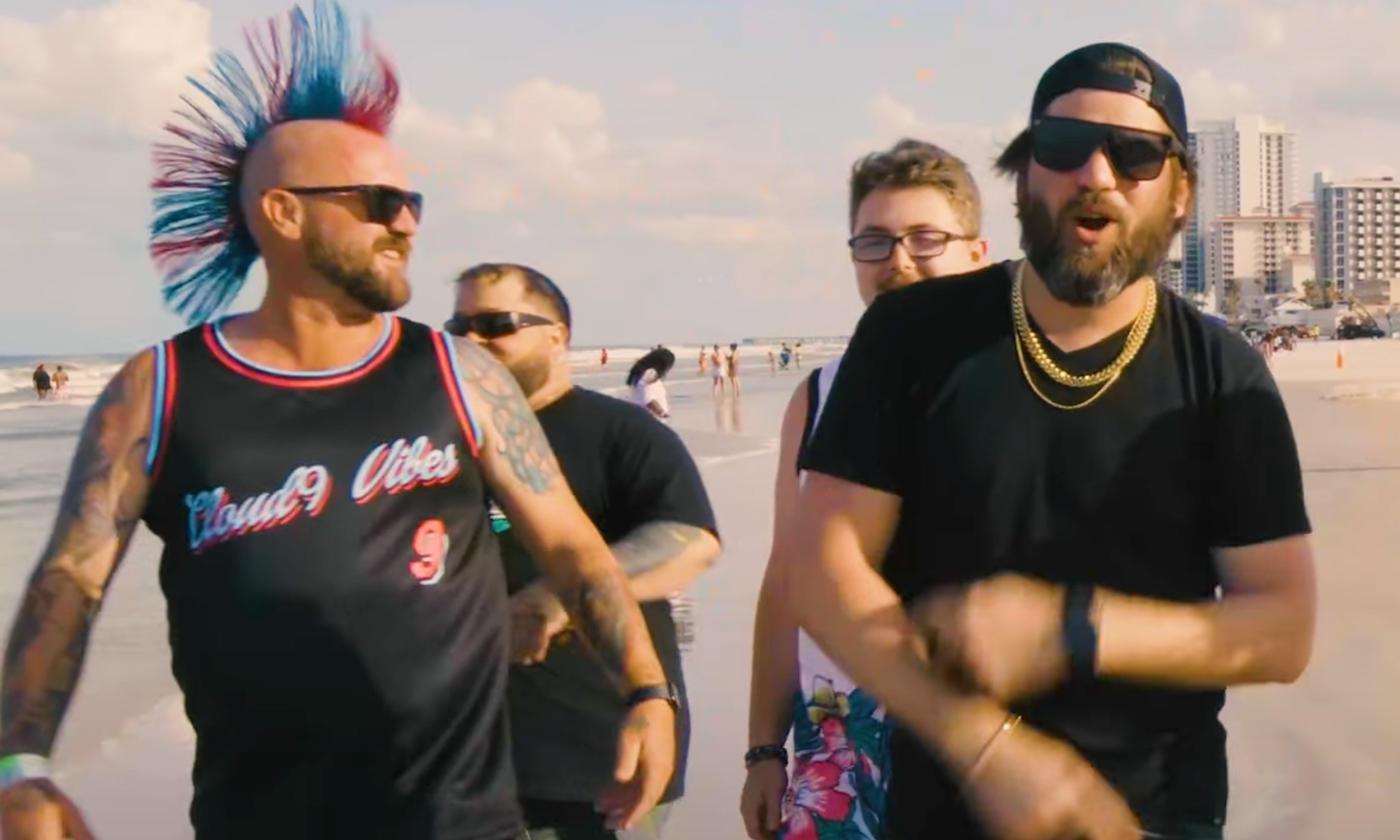 Members of Cloud 9 Vibes stroll down a beach as they perform a song together.