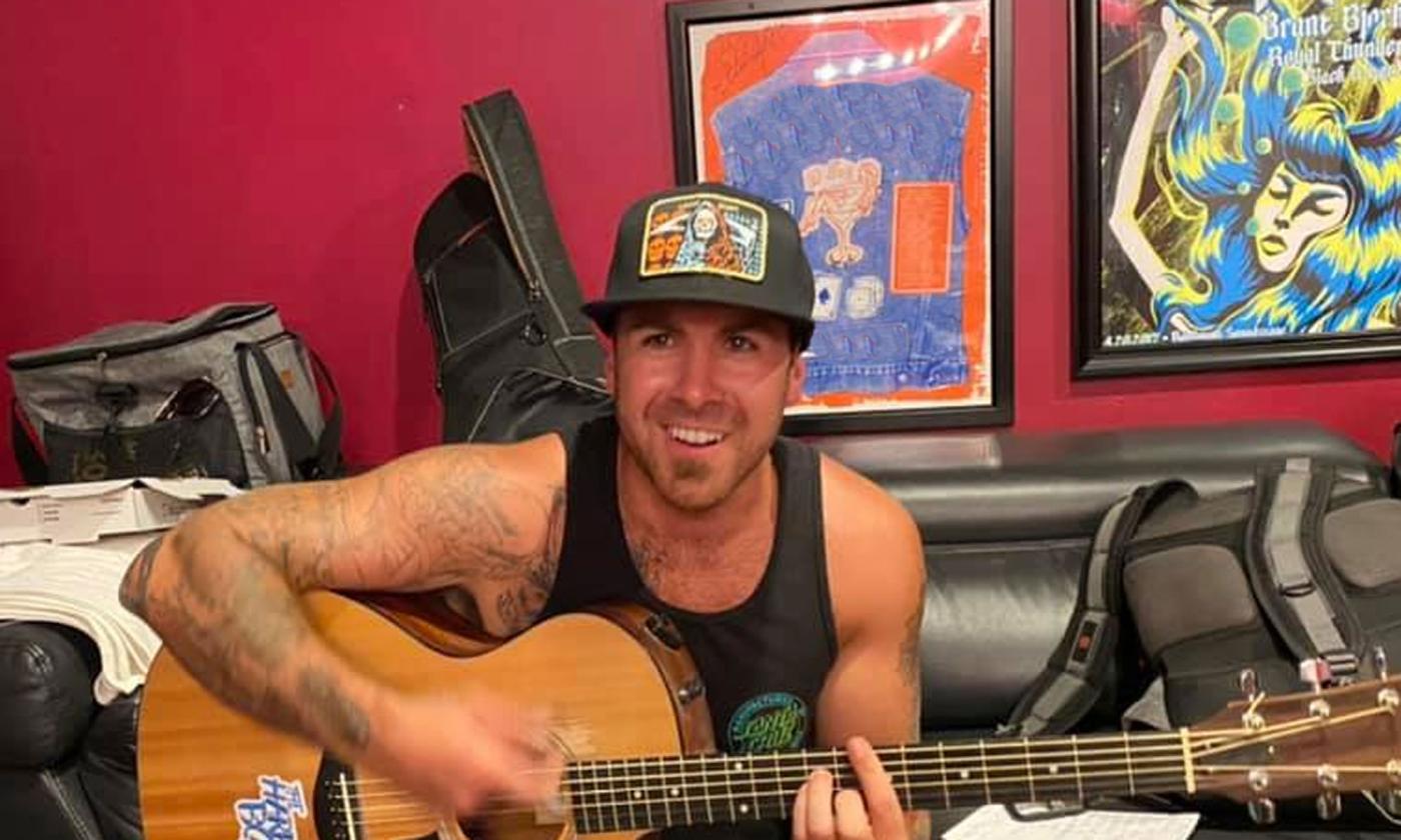 Musician Kyle Smith smiling, and playing a guitar, in a music studio