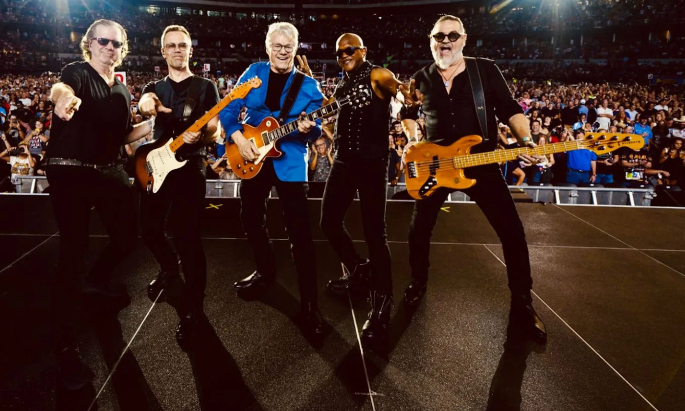 Bandmates from the Steve Miller Band pose on stage with their guitars.