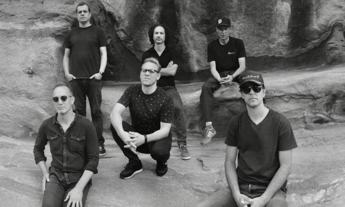 Bandmates from Umphrey's McGee sit on rocks while posing in dark clothing and glasses.