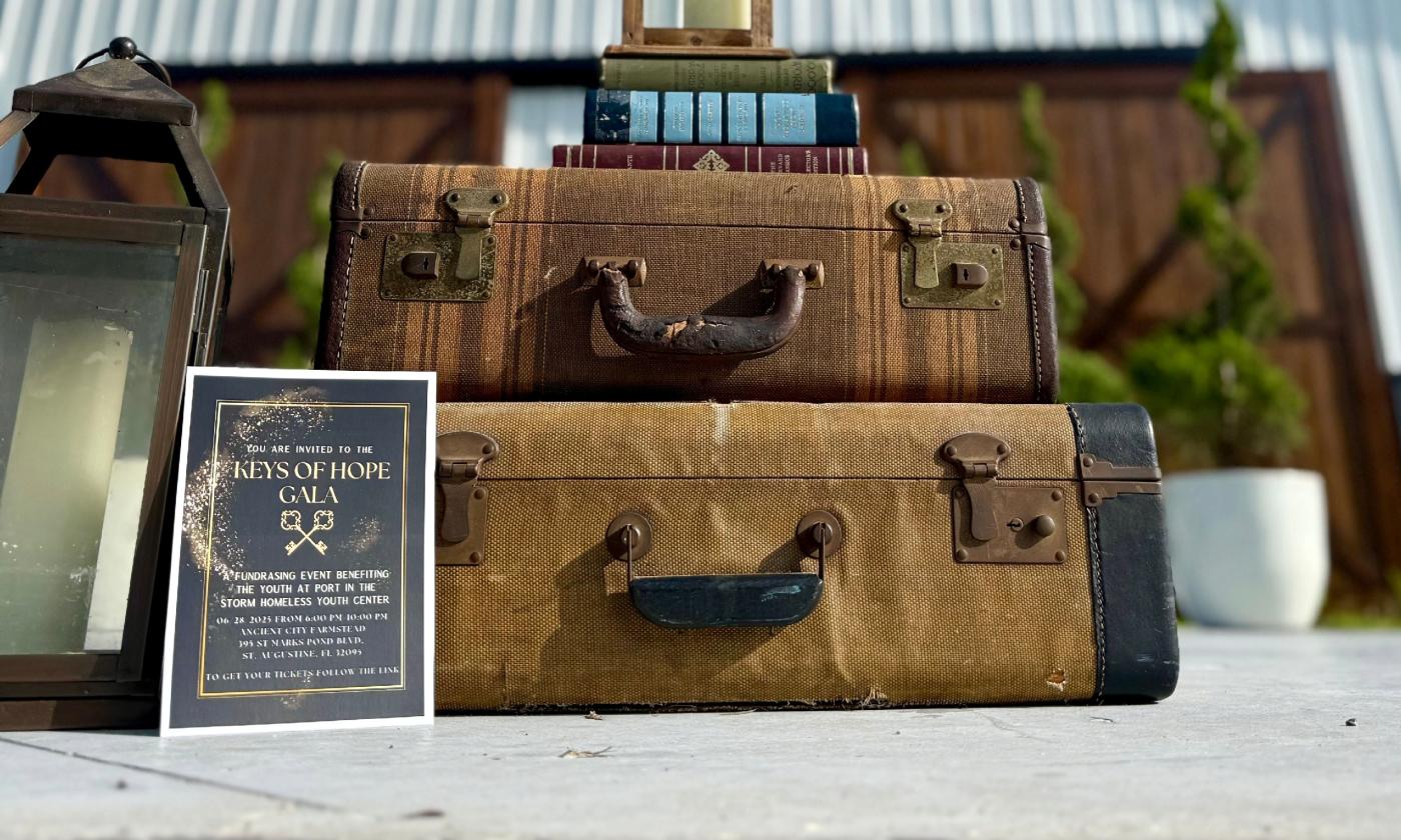 Two old suitcases topped by books promoting a gala for unhoused youth