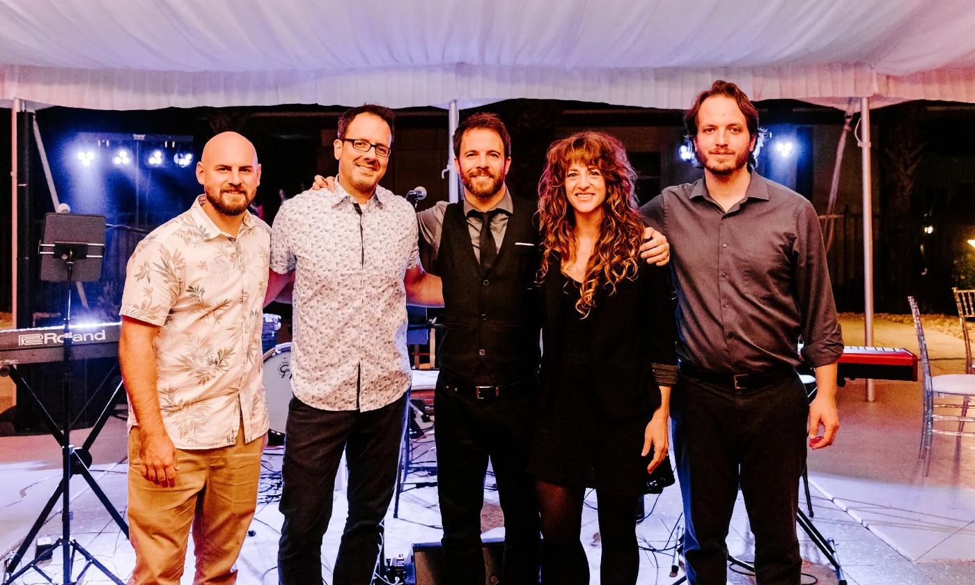 Five band members, standing shoulder to shoulder before a reception