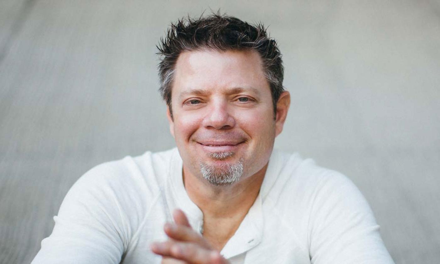 Songwriter Rodney Clawson, smiling, sitting in front of a white wall