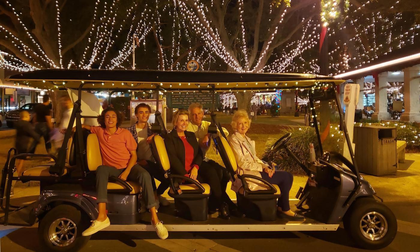 Guests aboard an electric vehicle, sitting by a decorated tree during St. Augustine's Nights of Lights