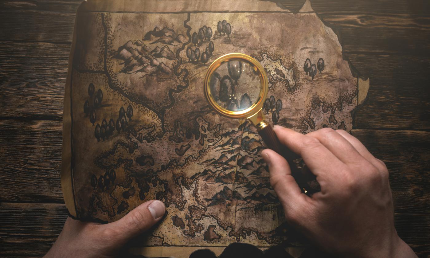 two hands holding an old map, one hand has a magnifying glass